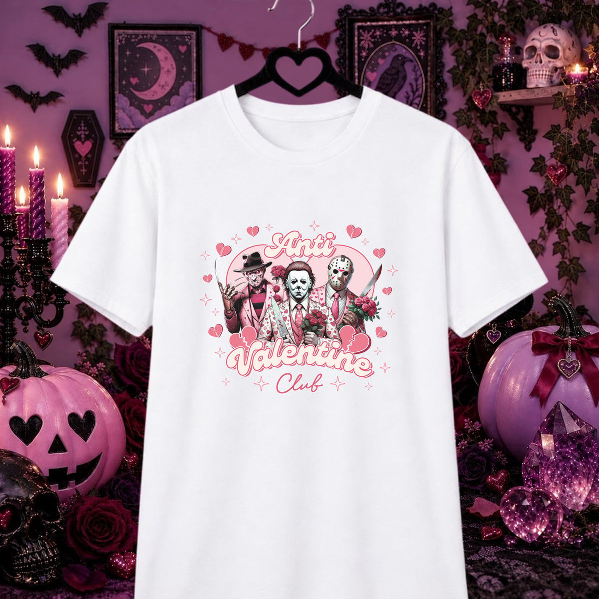 A white short-sleeve graphic T-shirt hanging on a black hanger against a Halloween-themed purple background. The shirt features a pink and black graphic of three horror characters with hearts and the words 'Anti Valentine Club'.