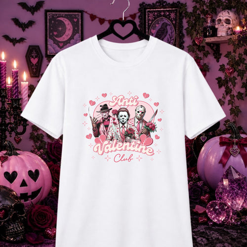 A white short-sleeve graphic T-shirt hanging on a black hanger against a Halloween-themed purple background. The shirt features a pink and black graphic of three horror characters with hearts and the words 'Anti Valentine Club'.