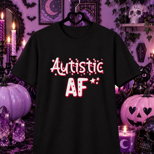 A black short-sleeve t-shirt hanging on a black hanger, featuring the text 'Autistic AF' in a white retro font with red outlines and small red stars. The shirt is displayed against a dark, spooky Halloween-themed background with purple pumpkins, candles, and a skull.