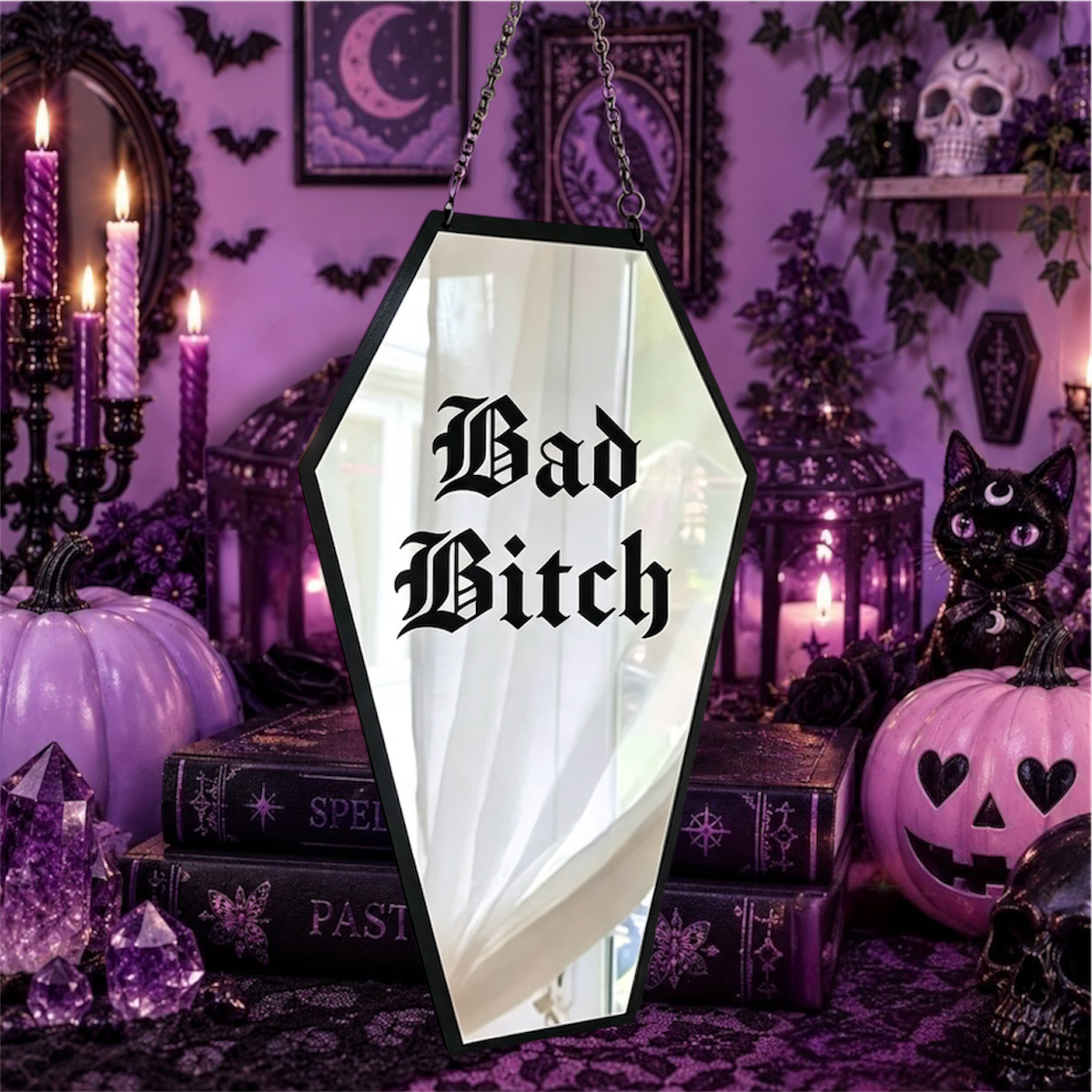 A coffin-shaped Halloween mirror with a black frame hanging in a spooky purple-themed room. The mirror reflects a white curtain, and the words 'Bad Bitch' are printed in black gothic font on the front.