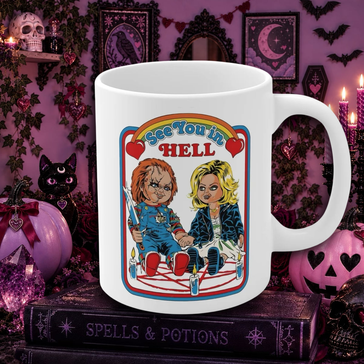 A white ceramic mug with a colorful cartoon-style graphic of Chucky and Tiffany in costumes under a rainbow that reads 'See You in HELL,' set on a dark decorative tabletop with pumpkins, candles, and gothic wall decor in the background.