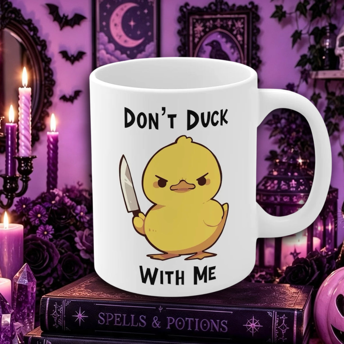 A white ceramic mug with a cartoon yellow duck holding a knife and the text 'DON'T DUCK WITH ME', displayed on a gothic-themed background with purple candles, roses, and a 'Spells & Potions' book.