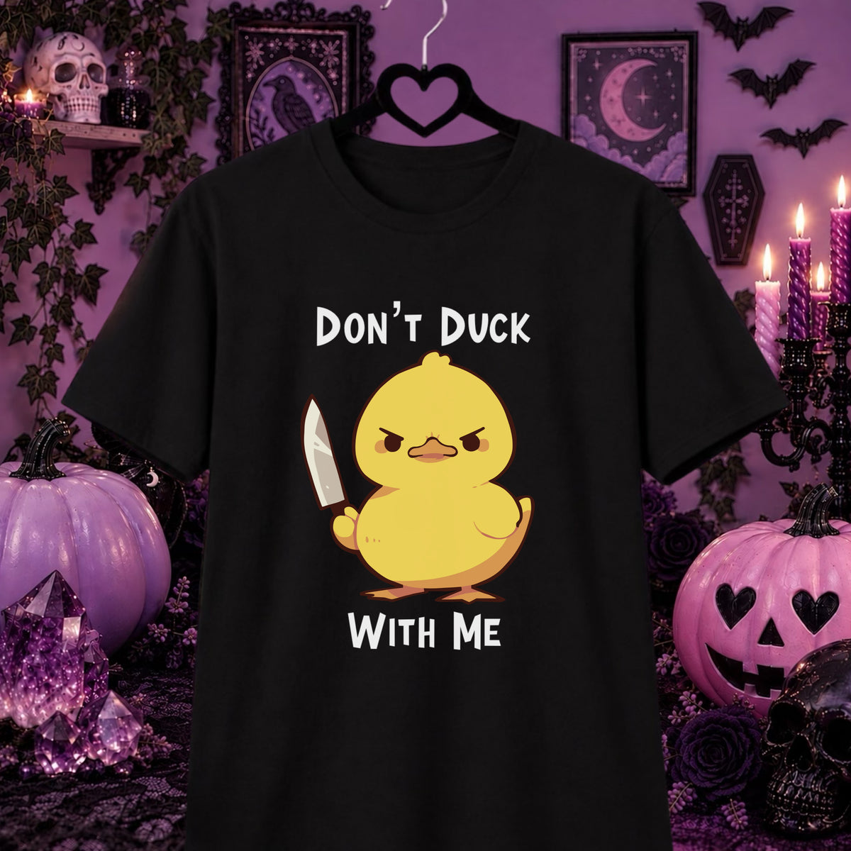 A black short-sleeve graphic t-shirt hanging on a black hanger against a Halloween-themed purple background. The shirt features a cartoon yellow duck holding a knife with the text 'DON'T DUCK WITH ME' in white.