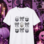 A white short-sleeve t-shirt on a black hanger, featuring a gothic-themed graphic print of Ghostface, Michael Myers, and bow designs. The shirt is displayed against a highly styled, dark purple Halloween-themed background with candles, pumpkins, and crystals.