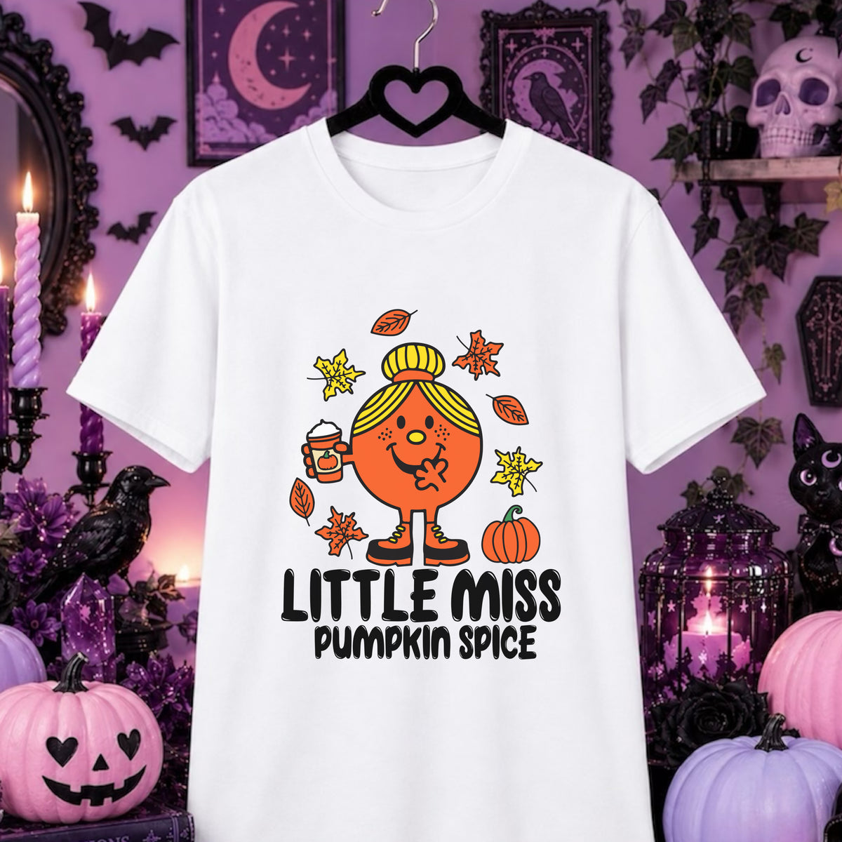 A white graphic t-shirt hanging on a black hanger against a purple Halloween-themed background. The shirt features a cartoon illustration of 'Little Miss Pumpkin Spice' with an orange face and body, yellow hair bun, holding a mug, surrounded by orange leaves and pumpkins, with the text 'LITTLE MISS PUMPKIN SPICE' printed below.