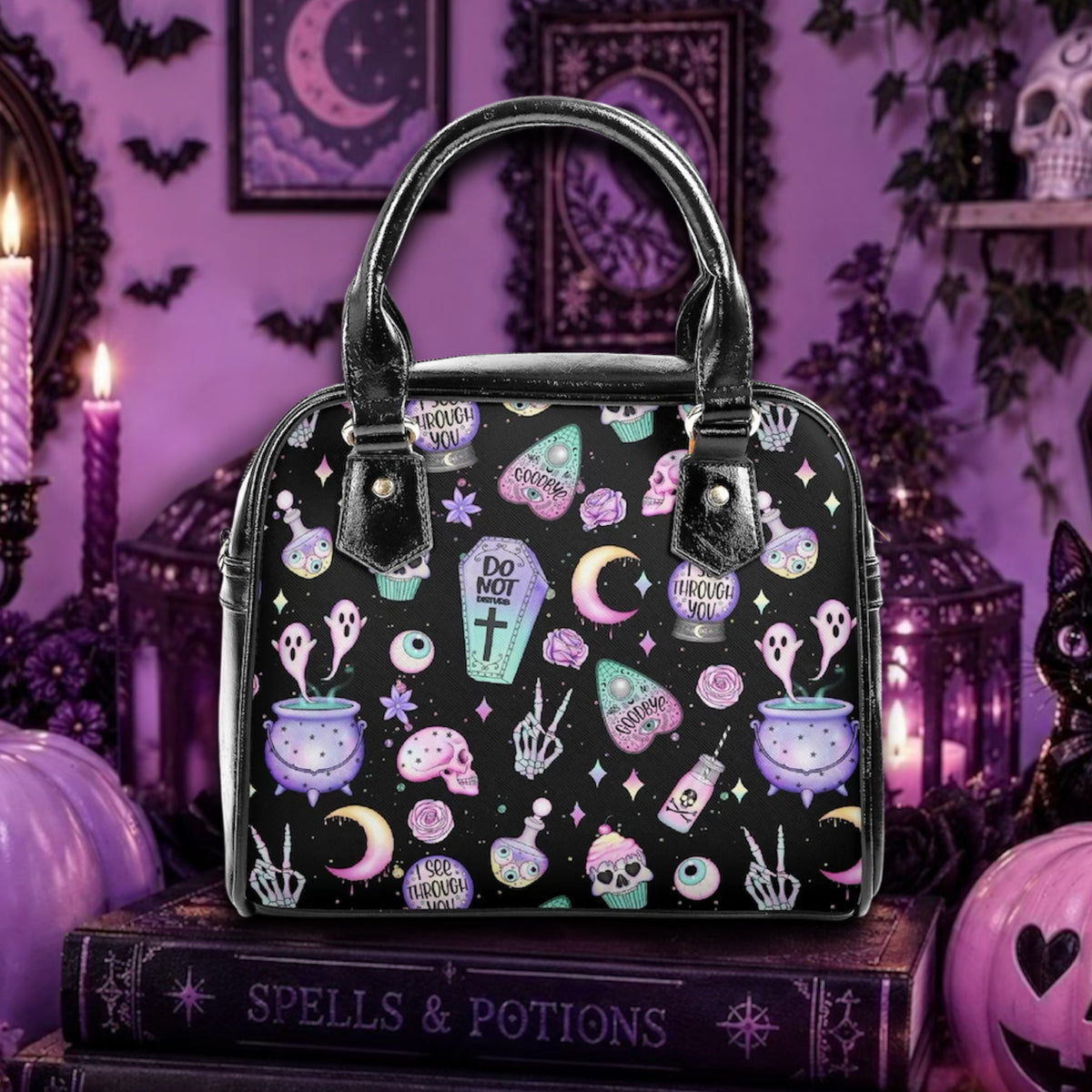 A black handbag with a colorful gothic pattern of cauldrons, ghosts, potions, and stars, displayed on a book in a Halloween-themed room.