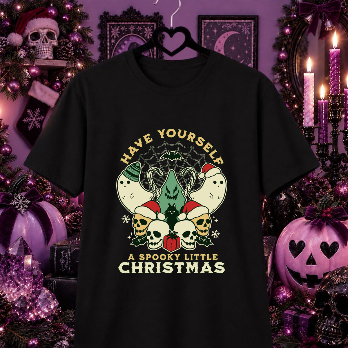 A black graphic t-shirt hanging on a hanger against a dark, festive Halloween and Christmas background. The shirt features a graphic design with the text 'HAVE YOURSELF A SPOOKY LITTLE CHRISTMAS' in a cream color, surrounding a central illustration of a green haunted tree, skulls, ghosts, and a Santa hat.
