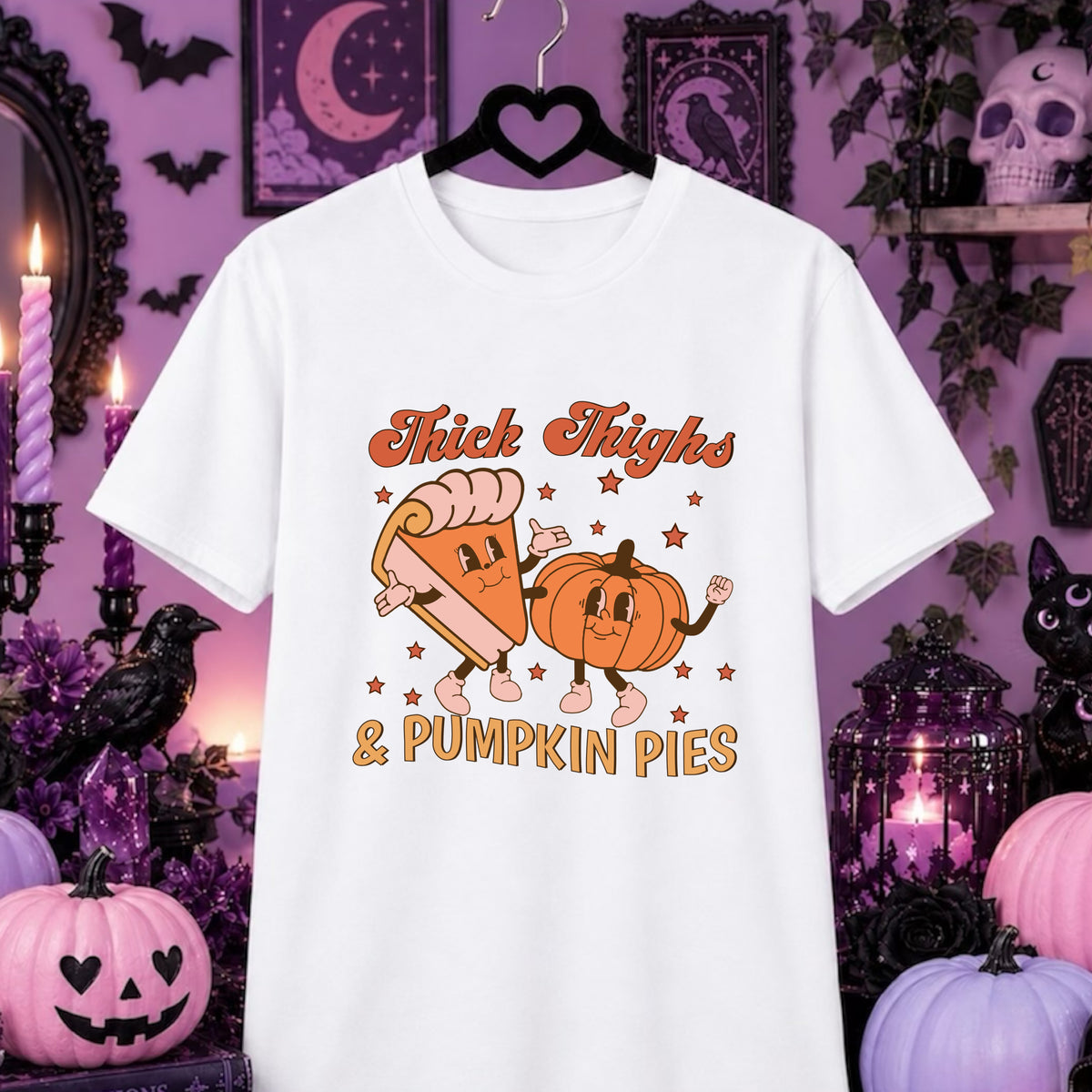 A white short-sleeve graphic T-shirt hanging on a black hanger against a Halloween-themed purple background. The shirt features a cartoon design of a slice of pumpkin pie and a pumpkin dancing, with the text 'Thick Thighs & Pumpkin Pies' in orange and yellow.