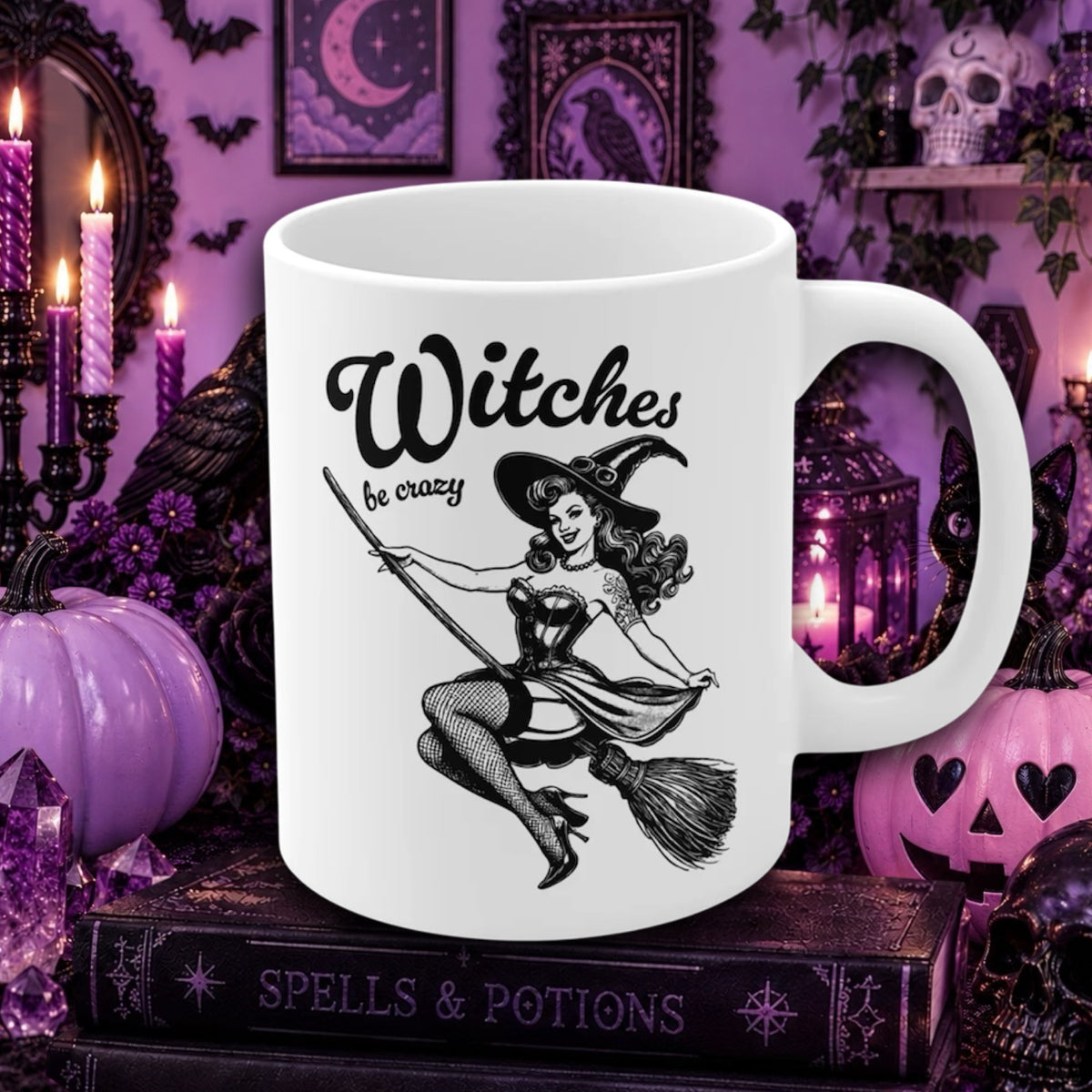 A Halloween white ceramic mug with a black vintage-style witch illustration and the text 'Witches be crazy,' displayed in a Halloween-themed purple setting with candles, pumpkins, and gothic decor.